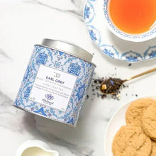 Earl Grey tea tin with lid beside teacup and scattered tea leaves