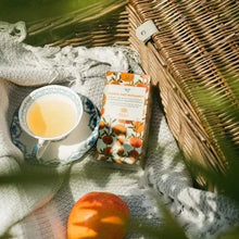 Tea bag sachet with dangling tag on fabric, beside a cup of brewed tea