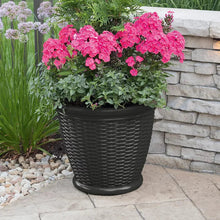 Dark gray wicker-style decorative planter with pink flowering plants, round ribbed design