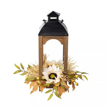 Wooden lantern with black top and glowing glass, topped with daisy and greenery