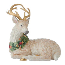 Resting deer figurine, light beige, with antlers and a green berry wreath around its neck.