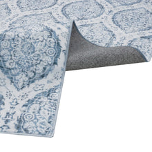 Corner edge of indoor area rug with light blue pattern and gray border backing