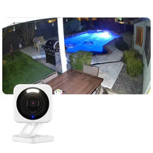 White outdoor security floodlight camera with illuminated lens, shown in a yard at night
