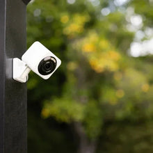 White outdoor security camera with two floodlight heads mounted on a dark post