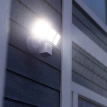 White security floodlight camera illuminating a siding wall at dusk