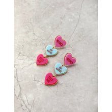 Valentine candy heart earrings laid flat: pink XOXO, blue BE MINE, and magenta KISS ME hearts.