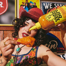 Hot sauce bottle held at the table, squirting sauce onto food