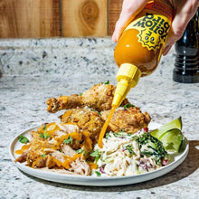 Hot sauce bottle drizzling over a plate of chicken, salad, and greens