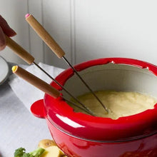 Red cast iron fondue pot with wooden forks and glass lid on black burner