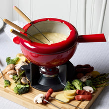 Red cast iron fondue pot with lid and wooden forks on black burner base