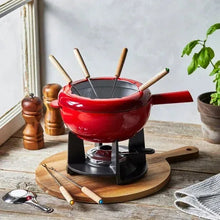 Red cast iron fondue pot with five wooden forks on black burner and round stand
