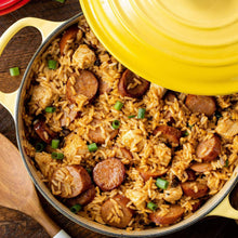 Yellow-lidded pot of jambalaya with rice, sausage slices, and green onions.