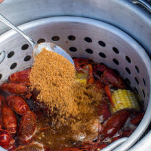 Crawfish boil pot with seasoning over shrimp, crawfish, sausage, and corn