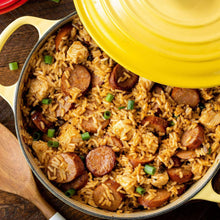 Jambalaya rice with sausage and herbs in a skillet, yellow lid partially open