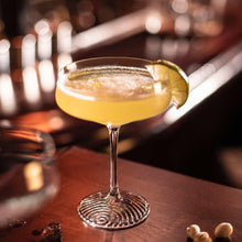 Coupe cocktail glass with golden drink and citrus garnish on the rim.