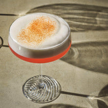 Coupe cocktail glass with frothy drink and fine orange garnish on top.