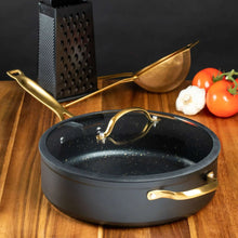 Black non-stick sauté pan with glass lid and gold handles on wood counter