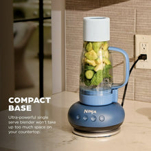 Personal blender with clear jar filled with chopped vegetables, blue base on countertop.