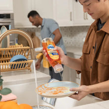 Orange antibacterial soap bottle while washing dishes, with foamy orange soap in bowl.