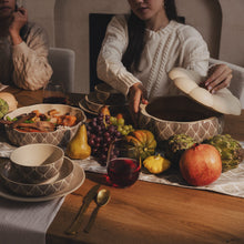 Stoneware soup tureen with cream lid and dark leaf-patterned body on table