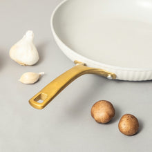 White ribbed fry pan with gold handle near garlic cloves and mushrooms