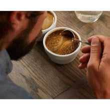 White coffee cup with brewed coffee and spoon, on wood table.