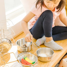 Child playing with stainless pots and pans and a colander on table