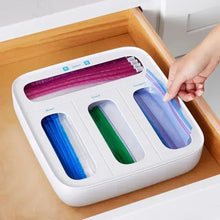 White food bag dispenser with four colored bag rolls in slots; hand holding one