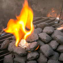 Fire starter cube burning among dark charcoal in grill
