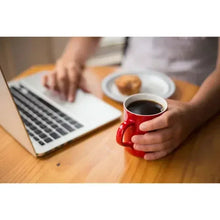 Red ceramic mug with dark coffee held by hands, with Keurig pod nearby