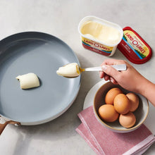 Hand spreading butter from canola oil tub; butter knife, small tub, and eggs nearby