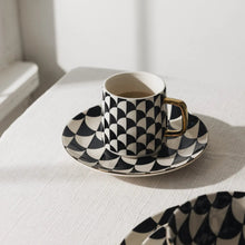 Black and white geometric stoneware mug with gold-tone handle on matching saucer