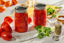 Wide-mouth mason jars with metal lids, filled with red preserves and herbs