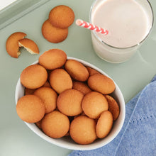 Vanilla wafer cookies in a white bowl, round golden cookies with a splash of milk