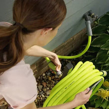 Lime-green garden hose looped near wall with spray nozzle and gray grip