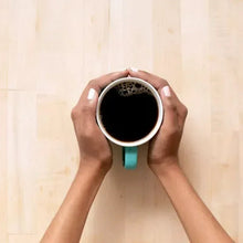 Hands holding a white-rimmed cup of dark coffee