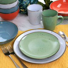 Green stoneware dinner plate with speckled glaze and gold rim, with bowls and mugs