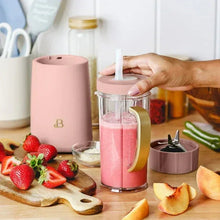 Rose personal blender pouring smoothie in clear jar with travel lid, hand placing lid