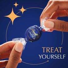 Hands opening a wrapped dark chocolate truffle, showing foil and shell