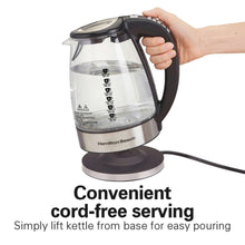 Electric glass kettle on a base with black handle, held by a hand