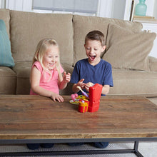 Children playing with Greedy Granny game toy, red chair and food pieces on floor