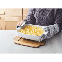 White ceramic oven-to-table serving dish on acacia board, carried with oven gloves