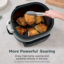 Sage green multi-cooker pot filled with browned chicken pieces, hand lifting lid