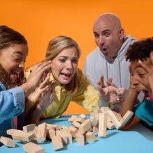 Family playing a wood block tower game with scattered light wooden blocks on a table