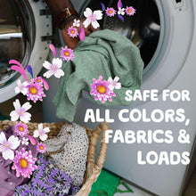 Laundry load with green scent booster bottle and fabric bundle near washing machine.