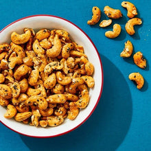 Seasoned cashews in white bowl with red rim, plus loose cashews nearby