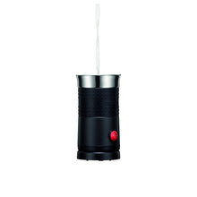Black electric milk frother with frothing whisk lifted above stainless cup