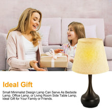 Small table lamp with black base and beige fabric shade beside a gift box.
