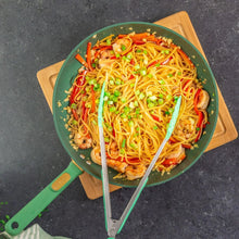 Green nonstick fry pan with noodles and shrimp on a wooden board