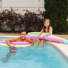 Pink and green pool swim noodles floating with two children in a backyard pool